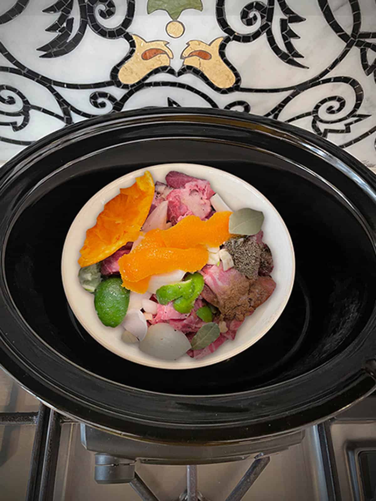Pork, orange, lime, onion halves and spices in a small bowl that is inside the large bowl of the slow-cooker