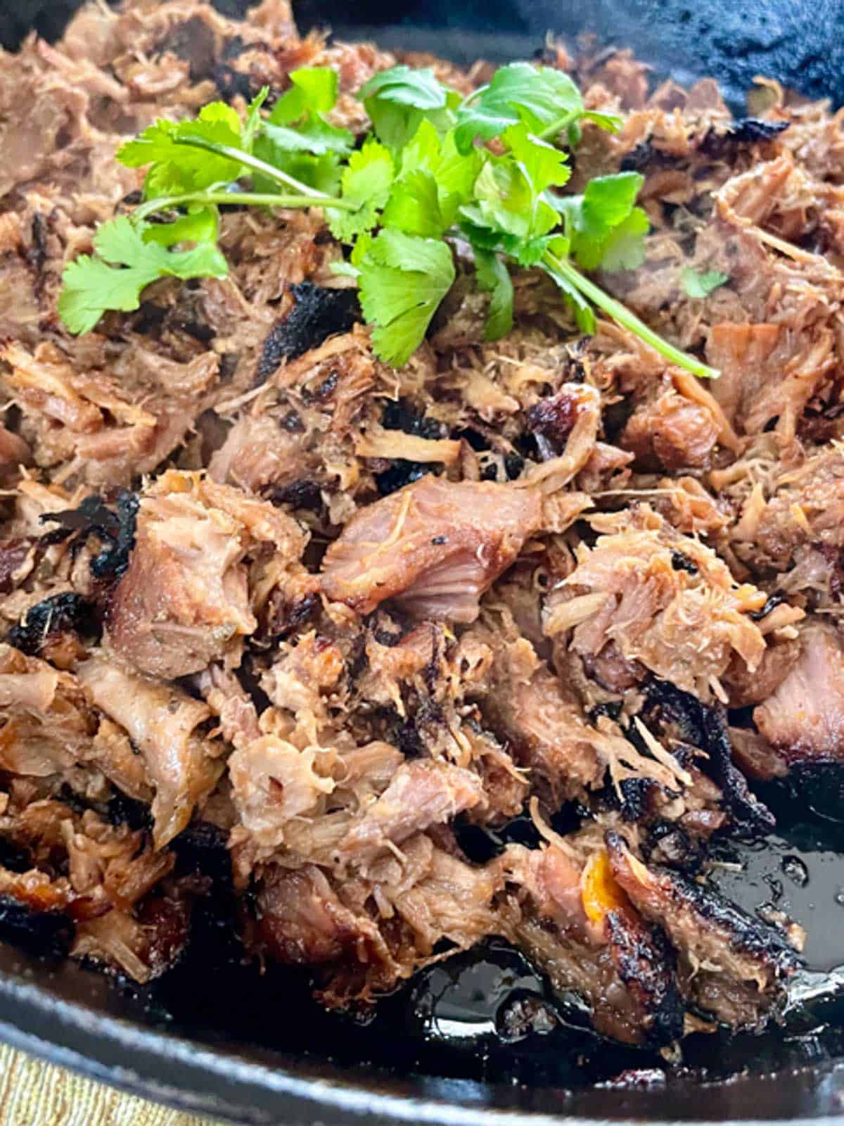 slow-cooker carnitas with a crispy exterior in a cast iron skillet garnished with cilantro