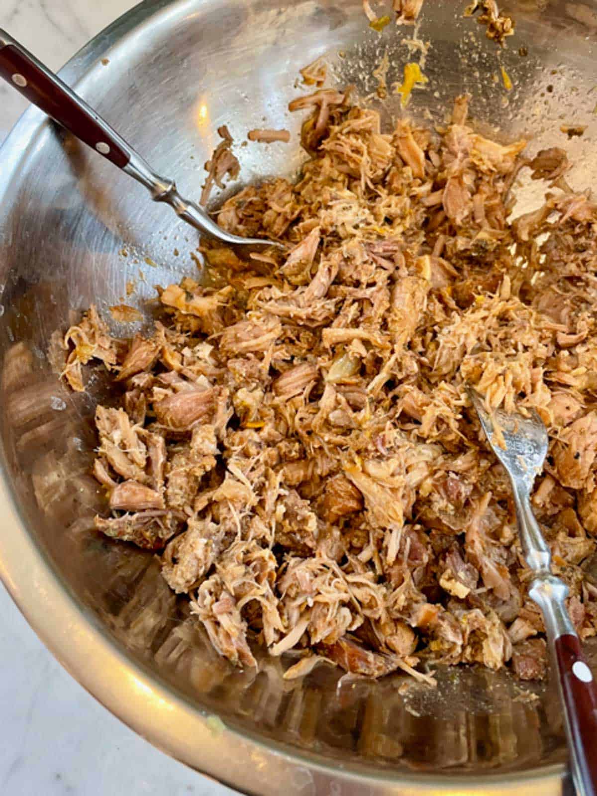 Pulling apart braised pork with forks in a large bowl