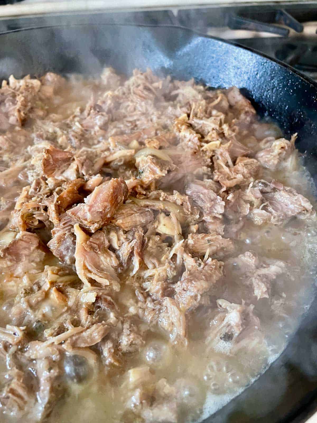 carnita meat in cooking liquid simmering in skillet