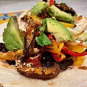 Open face tortilla topped with chipotle marinated portobellos, yellow and red peppers, and onion placed on a plate