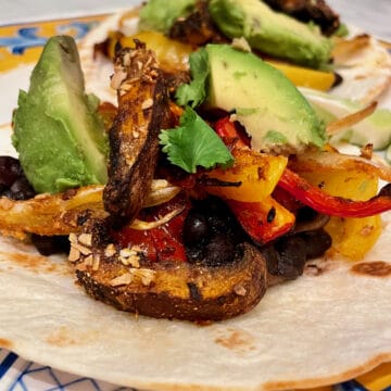 Open face tortilla topped with chipotle marinated portobellos, yellow and red peppers, and onion placed on a plate