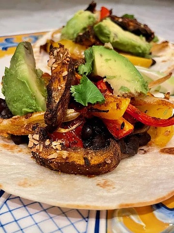 Open face tortilla topped with chipotle marinated portobellos, yellow and red peppers, and onion placed on a plate