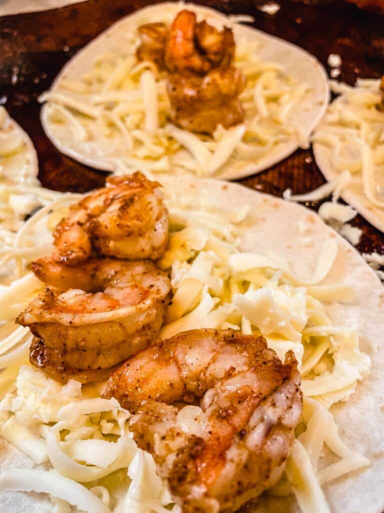 white corn tortillas topped with shredded Monterey Jack and spicy pan seared shrimp