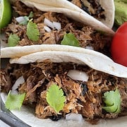 3 flour tortillas filled with pork carnitas meat garnished with cilantro and white onion