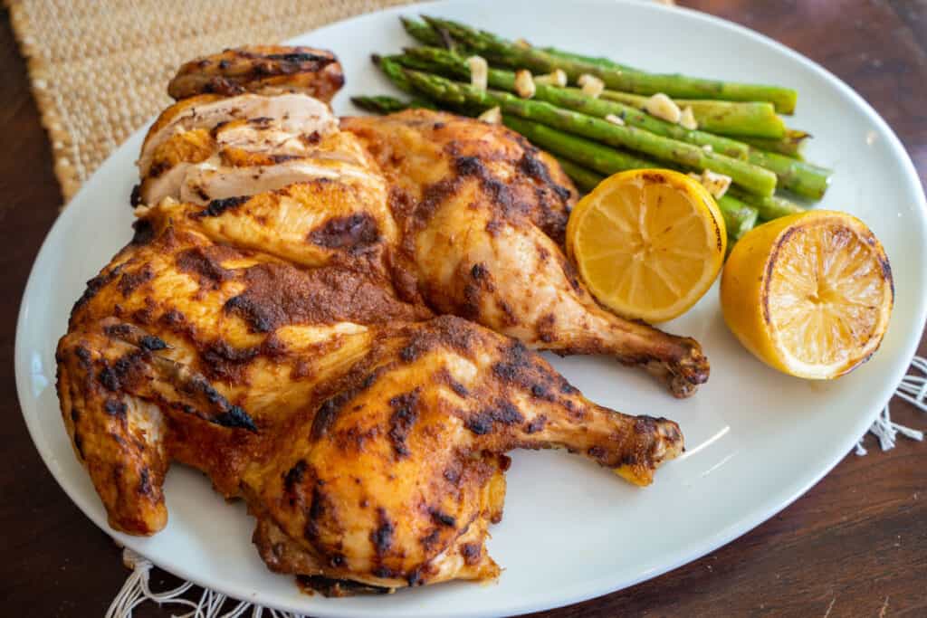 pepper and ginger spice rub on a roasted spatchcock chicken on a platter next to 2 lemon halves and asparagus with crispy garlic