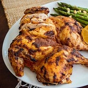 pepper and ginger spice rub on a roasted spatchcock chicken on a platter next to 2 lemon halves and asparagus with crispy garlic