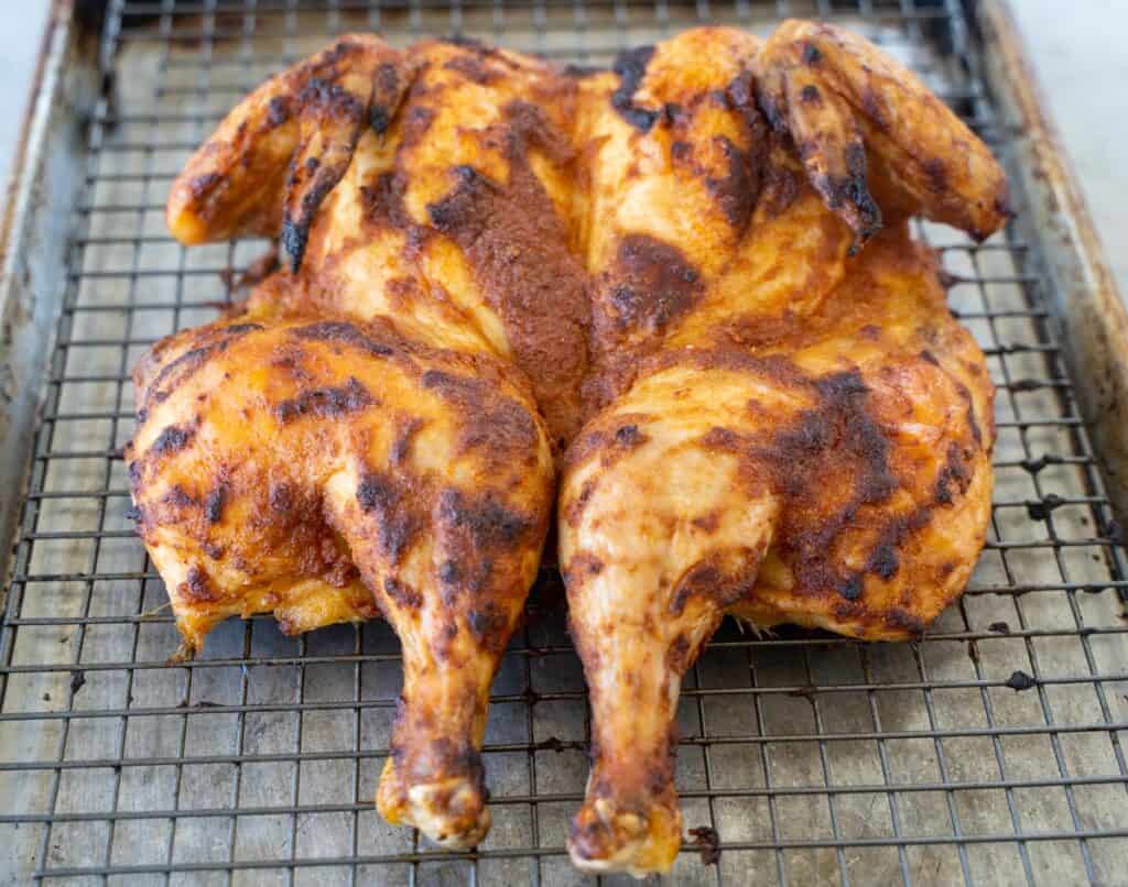 Crispy brown whole cicken sitting on a baking rack inside a rimmed baking pan