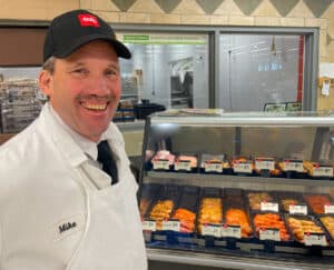 CUB Foods butcher in white coat and black baseball cap standing in front of meat counter