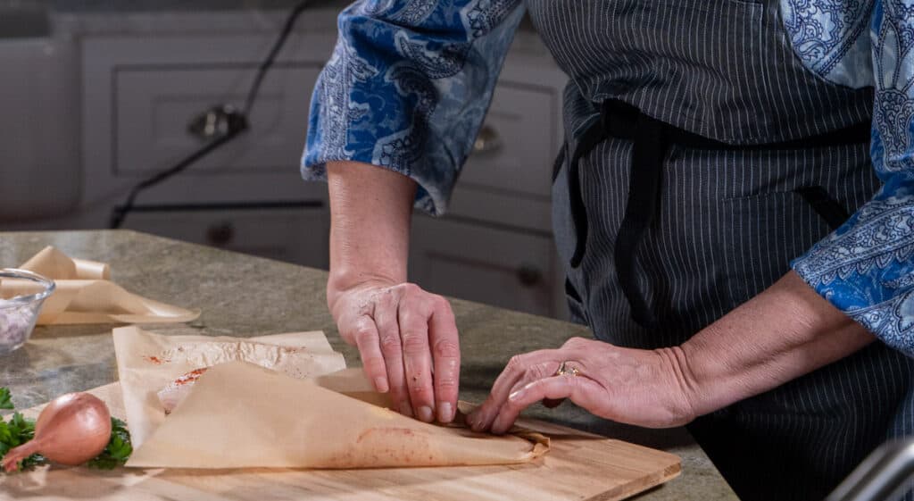 using 2 hands seal the parchment edges by folding the parchment paper in a tight pleated pattern