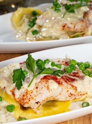 Baked Halibut on a bed of mushroom ravioli and a creamy alfredo sauce with green peas