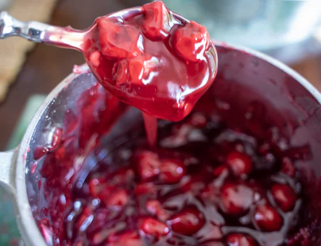 Thickened cherry pie filling in a sauce pan with a spoon showing the thick consistency and cherries