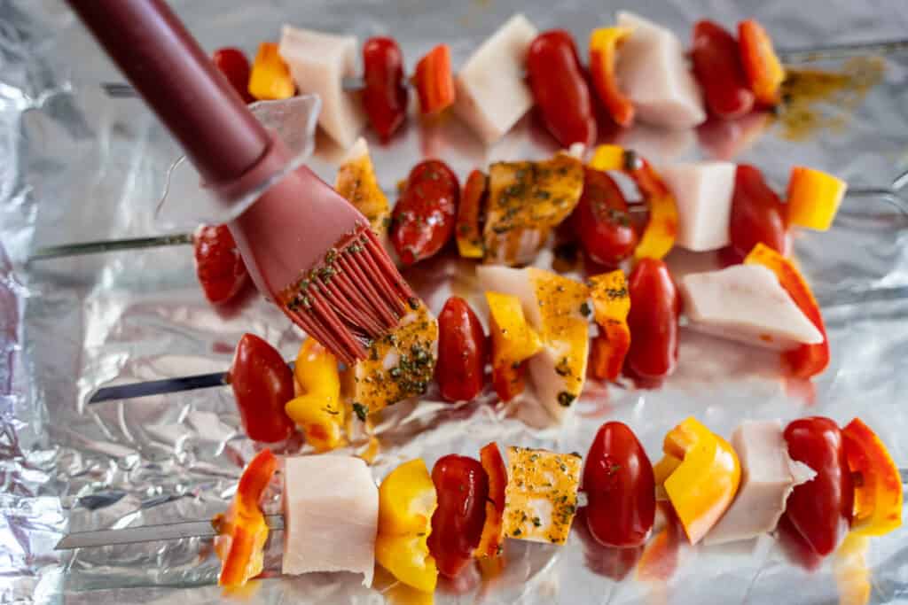 2 inch cubed swordfish, 2 inch diameter orange bell pepper slices, cherry tomatoes on metal skewers being brushed with marinade