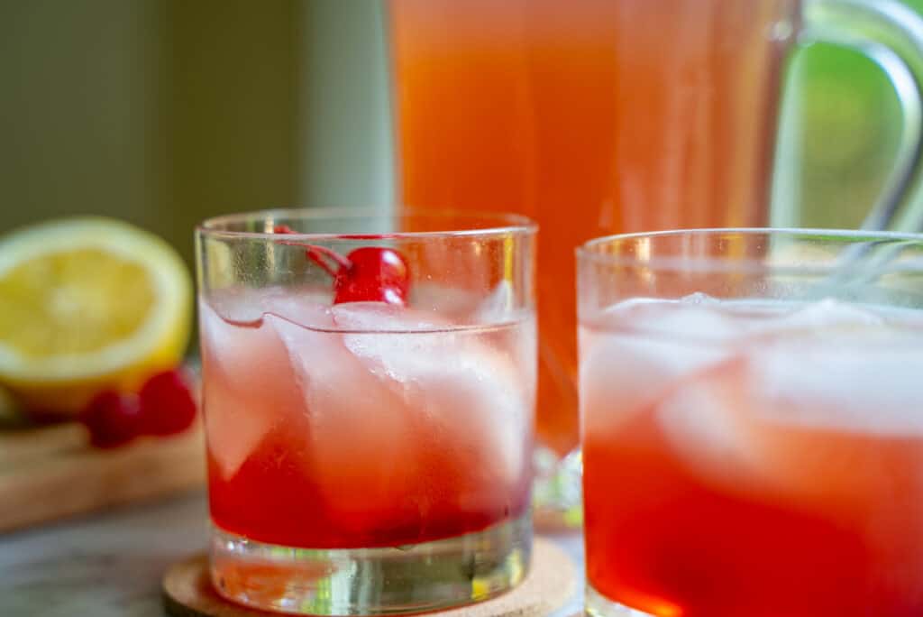 whiskey sour recipe poured over ice in 2 old fashioned glasses and topped with a maraschino cherry