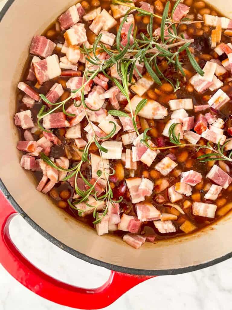 baked beans with uncooked diced bacon and sprigs of rosemary layered on top