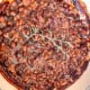 BBQ Baked Beans in a dutch oven with a sprig of rosemary