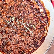 BBQ Baked Beans in a dutch oven with a sprig of rosemary