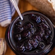 Blueberry jam in a mason jar, fresh blueberries in a white bowl and sourdough sitting on a table