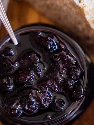 Blueberry jam in a mason jar, fresh blueberries in a white bowl and sourdough sitting on a table
