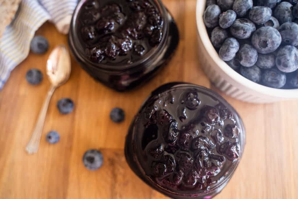 overhead shot of 2 mason jars filled with blueberry jam and a bowl of blueberries