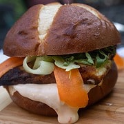 Sunday Dinner For Two Crispy Halloumi Burger on a pretzel bun with ribbons of carrot and cucumber slathered in a sweet chili mayo on a cutting board