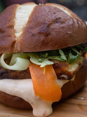 Sunday Dinner For Two Crispy Halloumi Burger on a pretzel bun with ribbons of carrot and cucumber slathered in a sweet chili mayo on a cutting board