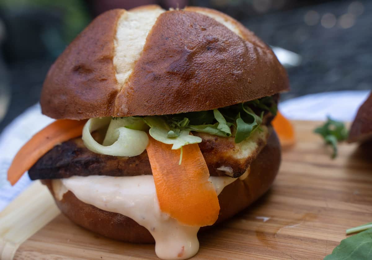 Sunday Dinner For Two Crispy Halloumi Burger on a pretzel bun with ribbons of carrot and cucumber slathered in a sweet chili mayo on a cutting board