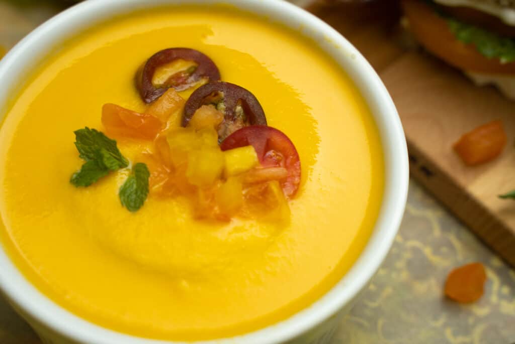 Gazpacho recipe with cantaloupe and sweet corn and a tomato, yellow pepper, cantaloupe, mint garnish in a bowl