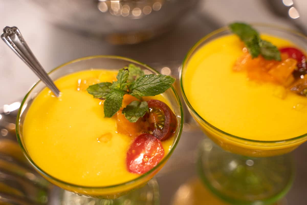 Gazpacho recipe with cantaloupe and sweet corn and a tomato, yellow pepper, cantaloupe, mint garnish in a green sherbert bowl