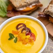 Cantaloupe and Sweetcorn gazpacho in a bowl alongside a BLT sandwich on a cutting boardn