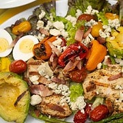 Grilled Pesto Chicken Cobb Salad on a white plate with balsamic vinaigrette being drizzled over the salad
