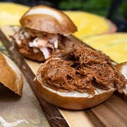 Slow cooker BBQ Pulled Pork on slider buns topped with a spicy slaw sitting on butcher paper and butcher block