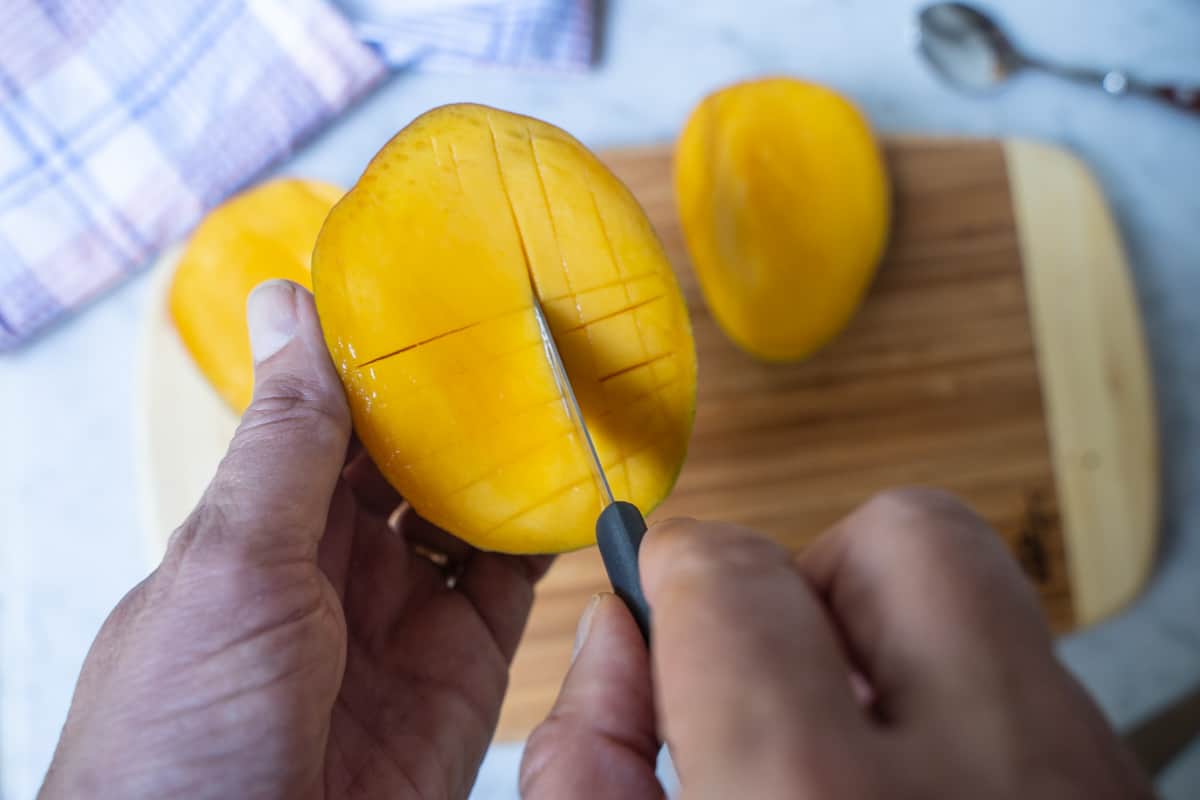 Slicing around the pit of a mango on a cutting board