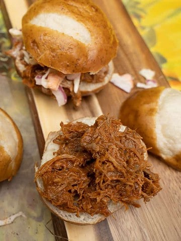 Slow cooker BBQ Pulled Pork on slider buns topped with a spicy slaw sitting on butcher paper and butcher block