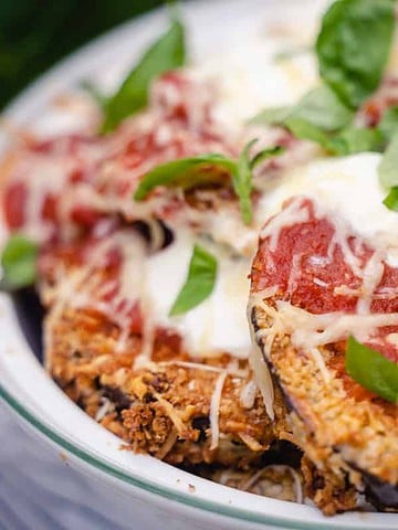 Eggplant parmesan for two in a white casserole dish garnished with basil