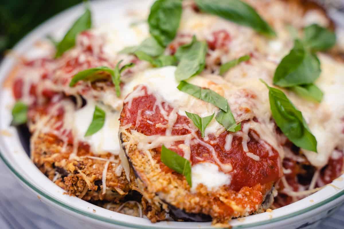 Eggplant parmesan for two in a white casserole dish garnished with basil