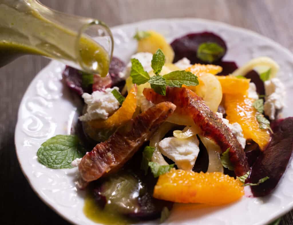 Roasted beet salad for two garnished with orange segments, picled fennel and a mint vinegar dressing on a white plate