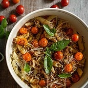 Roasted Cherry Tomato Pasta Recipe for two tossed with basil pesto, roasted garlic, roasted shallots and fried pepperoncini panko topping in a white pasta bowl surrounded by pints of cherry tomatoes