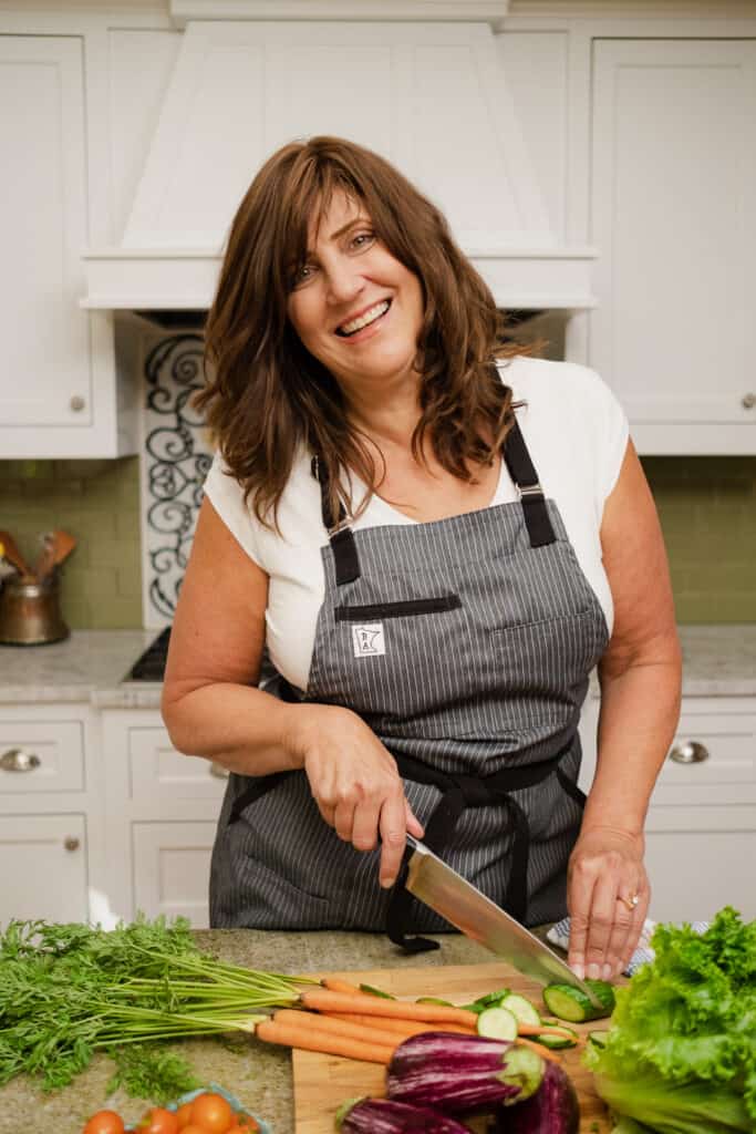 Women standing in front of kitchen counter cutting vegetables and smiling at the camera