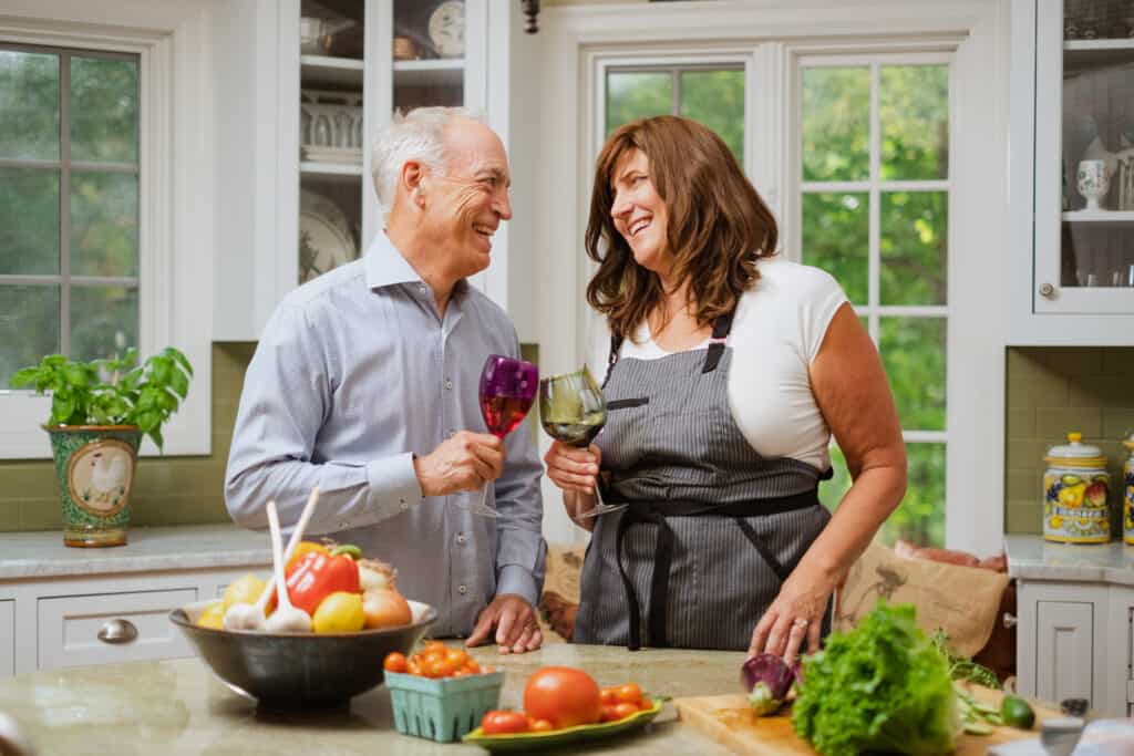 A man and a women standing in a kitchen drinking wine and chopping vegetables