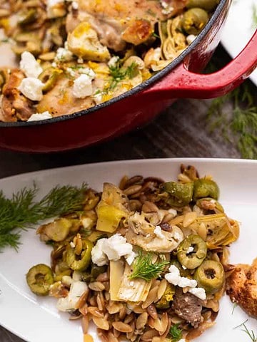 Easy one-pot chicken orzo recipe for two in a red dutch oven and on 2 white serving plates with dill, feta, artichokes and olives