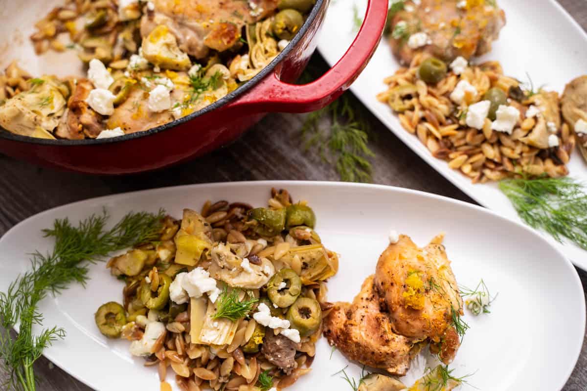 Easy one-pot chicken orzo recipe for two in a red dutch oven and on 2 white serving plates with dill, feta, artichokes and olives