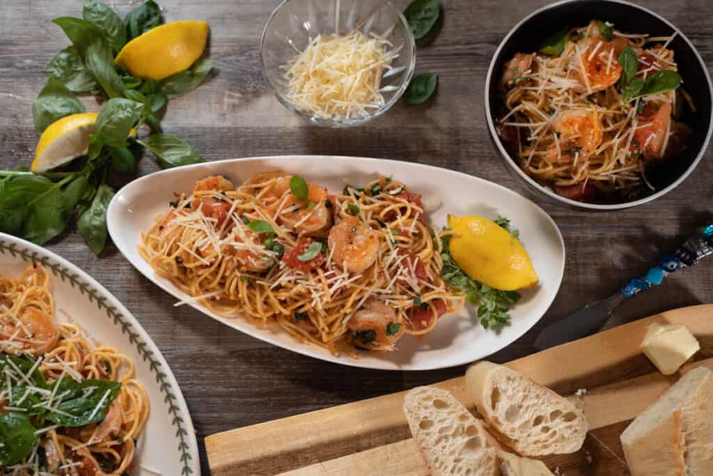 Easy Shrimp Pasta Recipe on a white plate and a black bowl, served alongside parmesan cheese and a warm loaf of bread