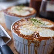 Baked lamb ragu with gnocchi in white ramakins on a wood table with a mason jar of ragu, garlic, parmesan and a cheese grater