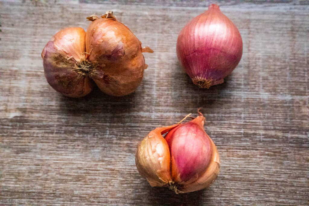 3 SHALLOT CLUSTERS SITTING ON A WOODEN TABLE