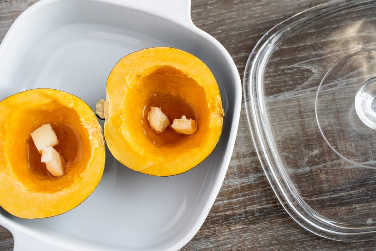 Acorn squash halves in a microwave safe bowl with butter and maple syrup in cavity