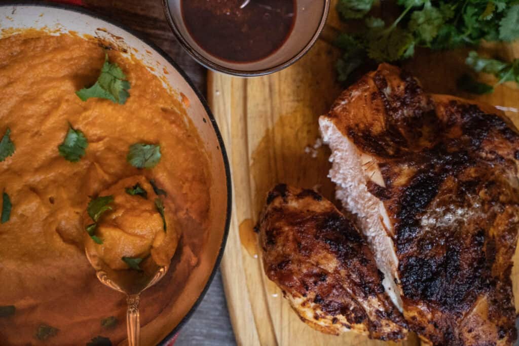 Turkey split breast on cutting board next to a pot of sweet mashed potatoes and a harissa sauce