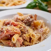 Proscuitto pasta with fresh tomatoes, mushrooms and cooked prosciutto garnished with parmesan cheese and lemon zest in a white bowl