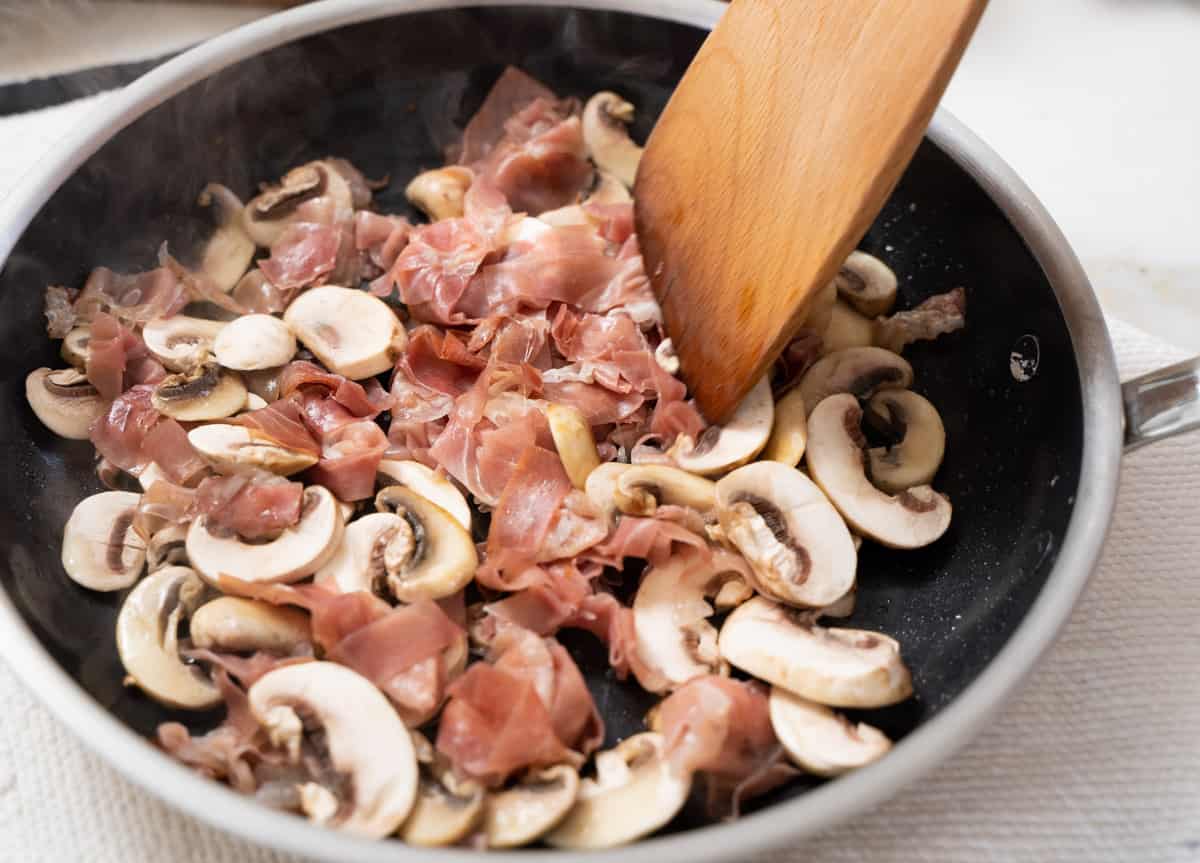 Prosciutto and mushrooms stirred with a wooden spoon