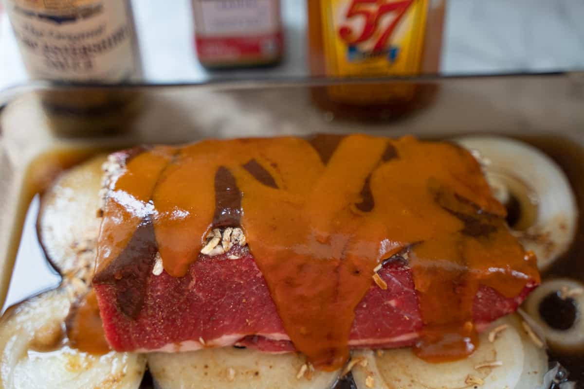 Sauces poured over the top of a beef brisket in a baking dish
